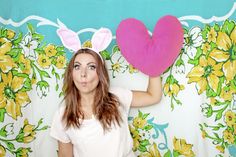 a woman holding up a heart shaped pillow in front of her face and wearing bunny ears