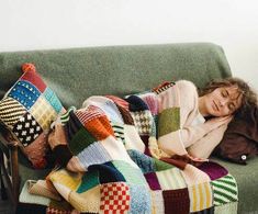 a woman laying on top of a green couch covered in a multicolored blanket