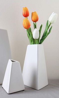 a white vase with tulips in it next to a laptop