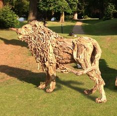 a sculpture of a lion made out of tree branches in a grassy area next to trees