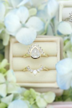 two engagement rings sitting in a box surrounded by flowers