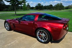 a red sports car is parked on the driveway in front of some grass and trees