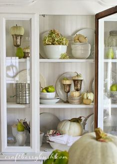 a white china cabinet filled with dishes and pumpkins