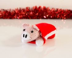 a knitted teddy bear wearing a santa hat on top of a white table next to red tinsel