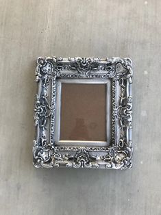 an ornate silver frame sitting on top of a cement floor next to a white wall