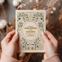 a person holding up a baby shower book in front of some flowers and branches with the words, baby shower alkendraa written on it