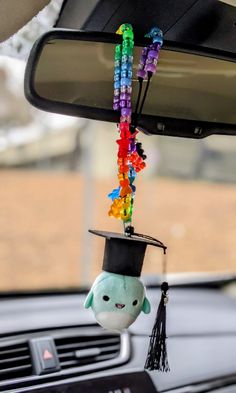 a stuffed animal wearing a graduation hat hanging from the dashboard of a car with beads attached to it