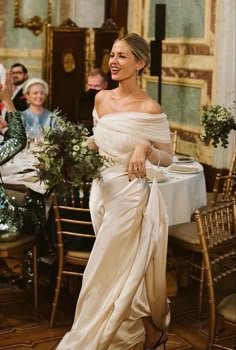 a woman standing in front of a table wearing a white dress and holding a bouquet