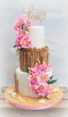 a three tiered cake decorated with pink flowers and bamboo sticks on a wooden table