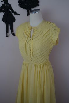 Description: Absolutely stunning 1940's summer dress and matching slip in a lovely light yellow color. Classic detailing includes pin tucking diagonal across the bust with 13 fabric covered buttons up the bodice. Neckline can be tied into a bow and the side closes with a metal zipper. The waist is gathered and there is a large 5 inch hemline on the skirt.  Fabric is sheer and photos are shown with the matching slip underneath. Measurements Dress Bust: 32/34 inches Waist: 26/27 inches  Length: 46 inches Measurements Slip Bust: 32 inches Waist: 32 inches  Length: 44 inches Size suggestion (but please go by posted measurements): Condition: Excellent condition with no real flaws to note. The slip has normal wear and some dents to the fabric, but outer dress only has some light staining on the Tuck Dress, Light Yellow Color, Outer Dress, Dresses 40s, Skirt Fabric, Design Clothes, Fabric Covered Button, Fashion Design Clothes, Button Dress