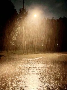 a street light shines brightly in the rain at night, as it rains down