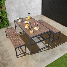 an outdoor table with two benches and plates of breakfast food on it, next to a brick wall