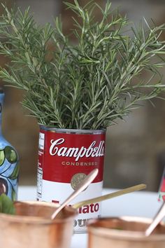 two cups with spoons are sitting on a table next to a can of soup