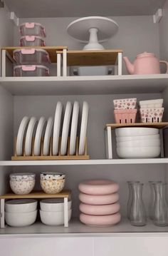 the shelves are filled with dishes, cups and other kitchenware in pink and white