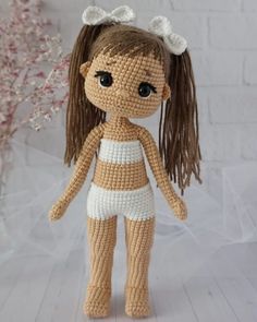 a crocheted doll is standing on a white surface with flowers in the background