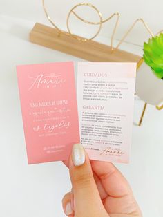 a person holding up a pink and white wedding program card in front of a plant