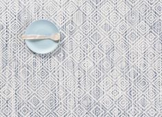 a blue and white place mat with a spoon on it, next to a plate