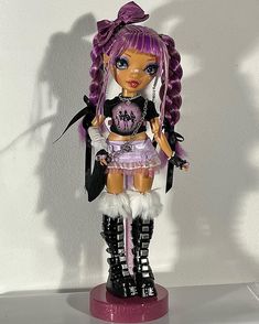 a doll with purple hair and black boots is standing on a white surface in front of a wall