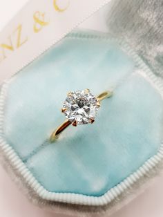 an engagement ring with a diamond in it on a blue velvet box and gold lettering