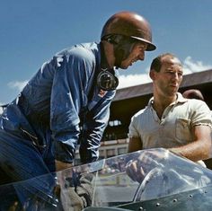 two men standing next to each other in front of a motorcycle and looking at something on the ground