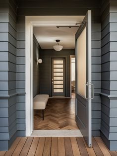 an open door leading into a room with wood floors and gray siding on the walls