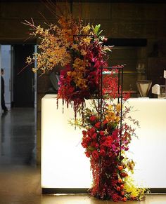 a tall vase filled with lots of flowers on top of a white table next to a wall