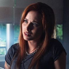 a woman with red hair and piercings in a dark room looking at the camera