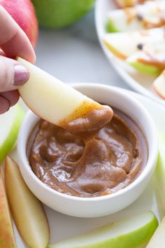 a person dipping an apple into a bowl of chocolate pudding with apples in the background