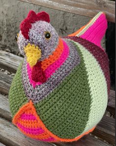 a crocheted stuffed chicken sitting on top of a wooden bench