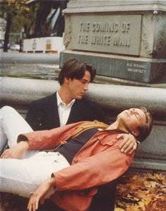 two people laying on the ground next to a monument and one is holding his head