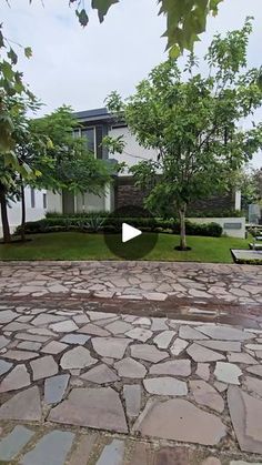 a stone walkway in front of a house with trees and benches on the other side