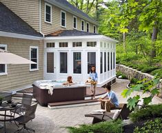 a man and woman sitting in an outdoor hot tub next to a patio with umbrellas