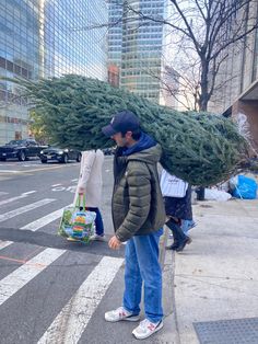 a man is carrying a christmas tree on his back while walking down the street in front of tall buildings