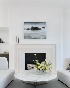 a living room with white furniture and a painting on the fireplace mantel above it