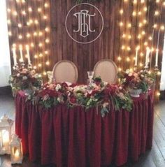 the table is covered with red cloths and decorated with flowers, greenery and candles