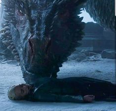 a man laying on the ground next to a large dragon in a snowy area with other people