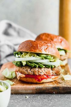 two burgers with lettuce and tomato on a cutting board