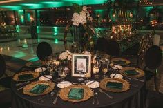 a black table topped with green and gold place settings next to a white framed photo