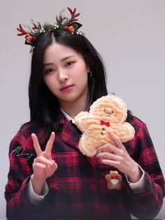 a girl holding a teddy bear and peace sign with her hands in front of her