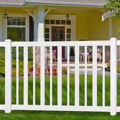 a white picket fence in front of a house with grass and flowers on the lawn