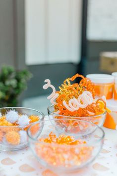 the table is set up with orange and white confetti in glass bowls on it