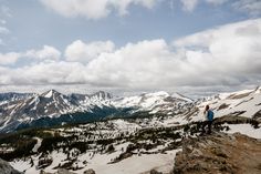 a man standing on top of a snow covered mountain with mountains in the back ground