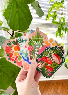 someone holding up some stickers in front of a potted plant with green leaves