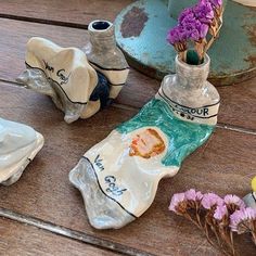 three ceramic vases with flowers in them sitting on a wooden table next to other items