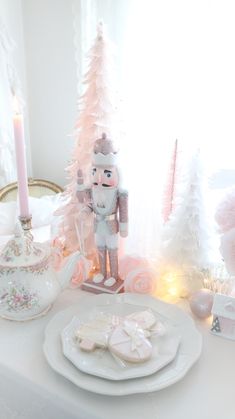 a white table topped with pink and white christmas decorations next to a teapot filled with cookies