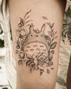 a woman's leg with a tattoo on it that has an image of a totoro and flowers