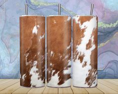 three brown and white cowhide tumblers sitting on top of a wooden table next to a wall