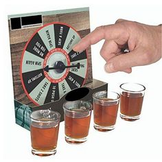 a hand is pointing at four shot glasses in front of a spinning wheel game set