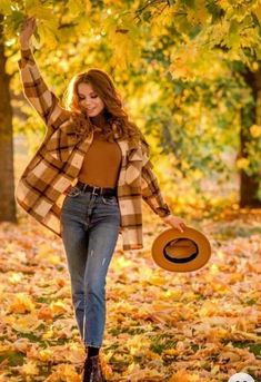 a woman is walking through the leaves with her hat