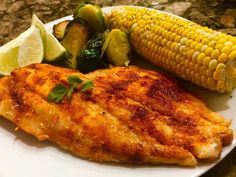 grilled fish, corn on the cob and vegetables are served on a white plate